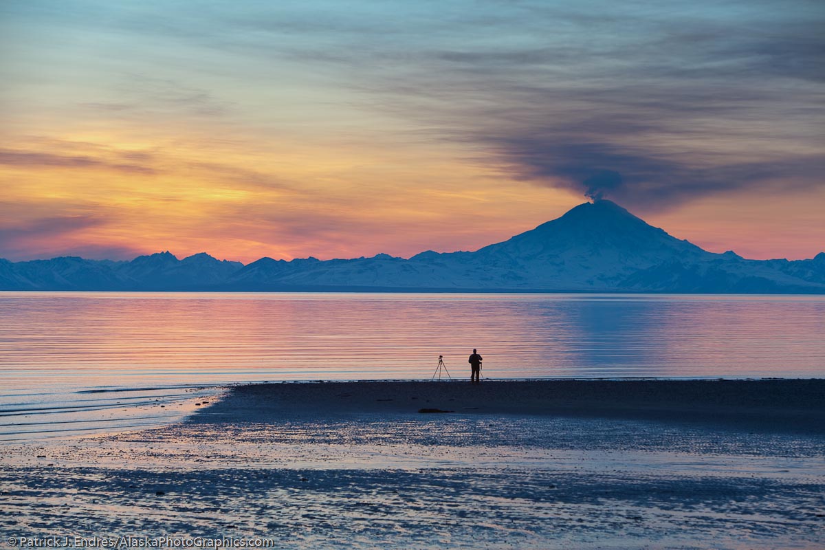 Photographer takes pictures of the plume of gas and vapor venting from the summit of Mt. Redoubt volcano (10,191 ft), of the Chigmik mountains, Aleutian range. View across Cook Inlet approximately 50 miles, at sunset, southcentral, Alaska.