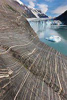 Layered sediments revealed in rock ground smooth by glacier weight and travel. Tidewater face of Cascade glacier and icebergs floating in Barry Arm, Chugach National Forest, Prince William Sound, southcentral, Alaska.